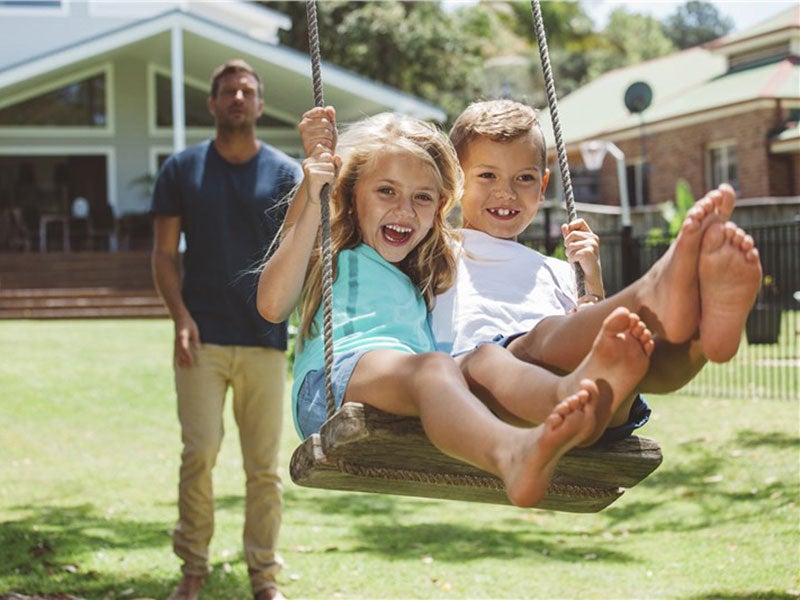 Two Girls swinging and a man standing behind 